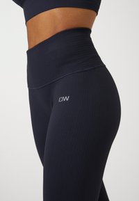 Granatowe rajstopy z prążkowanego materiału, z wysokim stanem i subtelnym logo. Tekstura jest gładka, zaprojektowana z myślą o komforcie i elastyczności.