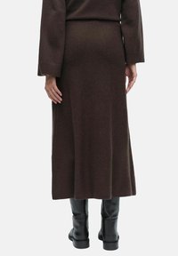 Ruskea neulottu midi-hame, jossa on suorasiluetti, hieman teksturoitu kangas ja helma, joka ulottuu kyynärpäiden alapuolelle. Hame on yhdistetty mustiin saappaisiin.