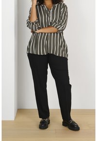Blouse à rayures vertes avec un léger éclat, détail bouton et manches retroussées, associée à un pantalon noir ajusté et des mocassins noirs épais.