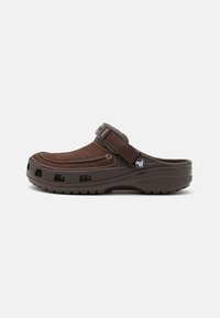 Sabot en cuir marron avec un dessus à texture douce, sangle ajustable et design perforé pour la ventilation. Semelle épaisse en caoutchouc pour l'adhérence.