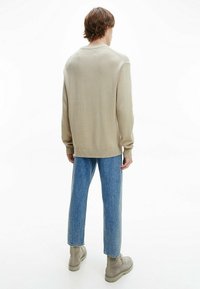 Pull beige en maille avec ourlet et poignets côtelés, associé à un jean droit bleu clair et des bottines beige. Tissu texturé visible.