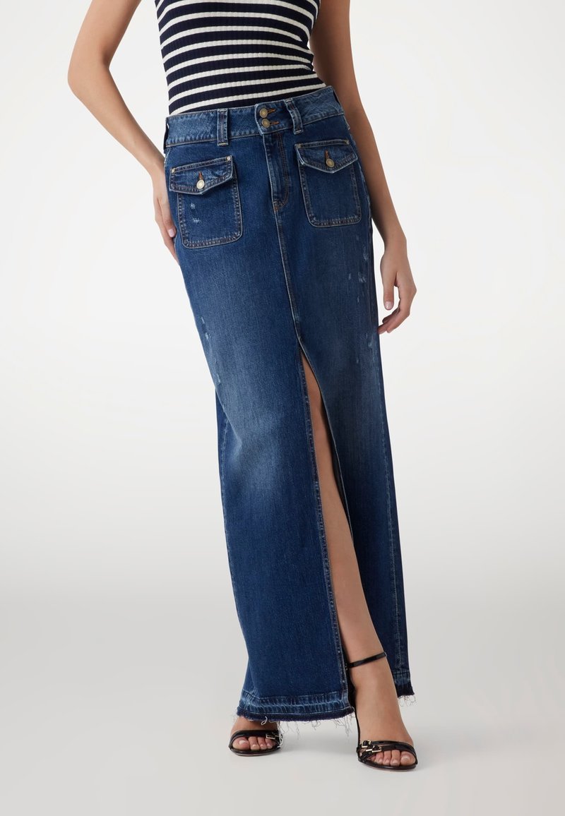 Tummansinisestä denim-maksihameesta, jossa on etuhalkio, kaksi suurta taskua ja purjehtinut helma. Yhdistetty mustien hihnasandaalien ja raidallisen paidan kanssa.