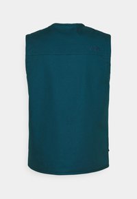 Mörk teal ärmlös väst med hög krage, visande bakperspektiv och subtilt broderad logga på övre högra axeln.