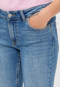 Blå denimjeans med en tettsittende fasong, høy midje og fem lommer. Har diskret sømmer og en sølvfarge knappelukking.