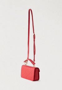 Crvena točkana kožna torba s odvojivim remenom za rame. Ima gornju dršku i zlatne ukrasne detalje. Pravokutnog je oblika.