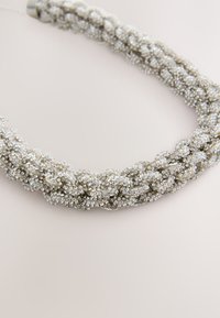 Silver braided necklace made of small, sparkling beads. Features a textured surface and a smooth metal clasp.