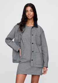 Must-valge ruudulise mustriga jakk, millel on tumesinine krae, esimesed nupud ja kaks küljetaskut; kantud sobiva kleidi kohal.