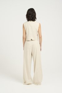 Beige mouwloze top en wijde broek van zachte, gestructureerde stof. De top heeft een split aan de achterkant, terwijl de broek discrete achterzakken heeft.