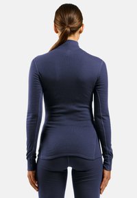 Navy long-sleeve shirt with a high neckline, ribbed texture, and fitted design, featuring flat seams and a slightly curved hem at the back.