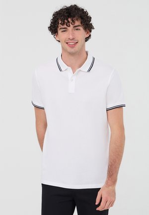 Maglietta polo bianca con colletto a righe bianche e nere e un'apertura a tre bottoni, maniche corte con polsini a righe coordinate. Tessuto morbido.