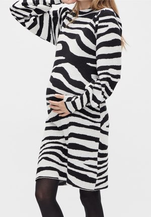 Sukienka dzianinowa z czarno-białym wzorem zebra, długimi rękawami i luźnym krojem, podkreślająca zaokrąglony brzuch.