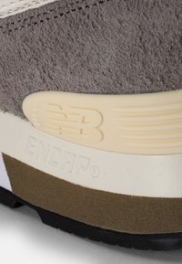 Tige en cuir suédé gris avec des accents crème, présentant une semelle en caoutchouc texturée et le logo "ENCAP" embossé sur le talon.