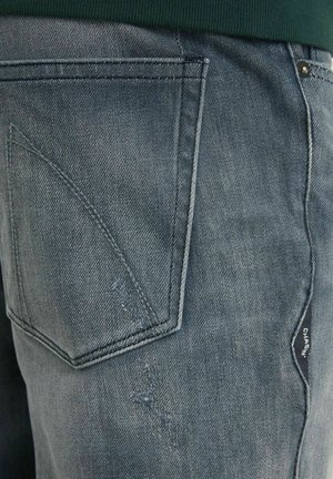 Nööpidega denimhüppajad, mis on pleekinud sinise värviga ja tekstureeritud viimistlusega, sisaldavad diagonaalset tagakaotust ja tootetagi külgedel.