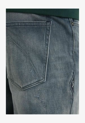 Fakó kék színű farmernadrág, texturált felülettel, ferde hátsó zsebbel és oldalán márkás címkével.