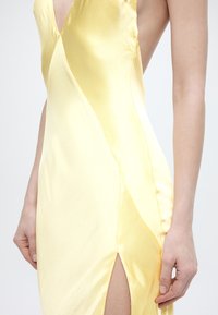 Κίτρινο σατεν φόρεμα χωρίς μανίκια με διαγώνια πάνελ και σκίσιμο μέχρι το μηρό, φορεμένο από άτομο με τα χέρια χαλαρά στο πλάι.