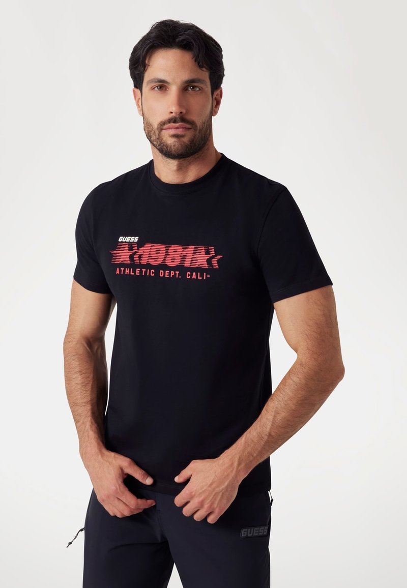 Black cotton t-shirt featuring a bold red graphic print with "GUESS 1981 ATHLETIC DEPT. CALI." Designed with a classic crew neckline.