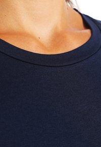 Marinblå bomullstyg med en slät textur, med en rundad halsringning och synlig söm längs fållen och halsringningens kanter.