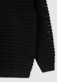 Manica di un maglione nero lavorato a maglia con motivo aperto orizzontale e polsino a coste su uno sfondo chiaro.