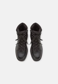 Bottines noires avec un dessus en cuir lisse, un col texturé, un laçage à l'avant et une semelle en caoutchouc robuste. Fermetures éclair sur les côtés pour un enfilage facile.
