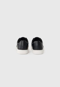 Zwarte leren sneakers met een gladde textuur, contrasterende witte rubberen zool en zichtbare stiksels. Achteraanzicht toont het hiel detail.