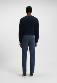 Granatowy sweter z okrągłym dekoltem, o prążkowanej strukturze, w połączeniu z jasnoniebieskimi spodniami. Buty mają czarno-białą kolorystykę. Widok z tyłu.