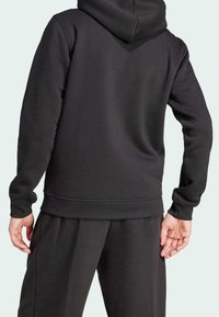 Černá mikina s kapucí vyrobená z měkké tkaniny, s klokaní kapsou, žebrovanými manžetami a stahovací kapucí. Jednoduchý design s volným střihem.