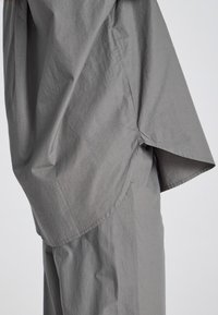 Top in tessuto grigio a vestibilità morbida con una texture rugosa, caratterizzato da un orlo asimmetrico e maniche corte e ampie.