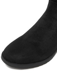 Stivaletto in suede nero con punta arrotondata e superficie liscia. Suola piatta in gomma, senza hardware o decorazioni visibili.