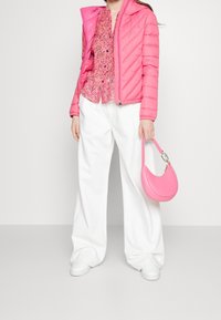 Veste rose rembourrée, blouse rose à fleurs, pantalon blanc à large jambe et sac à main rose assorti. Texture lisse, design décontracté. Chaussures blanches.