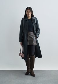 Abrigo de cuero negro, falda mini de cuero marrón, leggings negros, botas marrón hasta la rodilla y un pequeño bolso rosa. Diseño simple, textura suave.