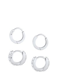 Boucles d'oreilles créoles Huggie en métal argenté, présentant des surfaces lisses et une paire ornée de petits cristaux transparents pour une touche de détail supplémentaire.