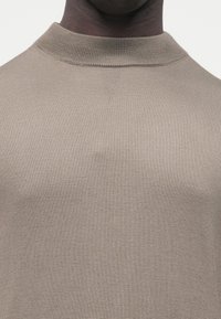 Beżowy sweter z dzianiny z golfem, o dopasowanym kroju, gładkiej fakturze i prążkowanym kołnierzu. Widok z bliska ukazuje szczegóły delikatnej tkaniny.