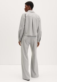 Veste grise ajustée avec un dos plissé, des manches longues et des poignets boutonnés, associée à un pantalon large gris assorti.