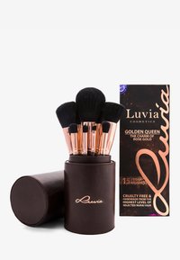 Set med 15 svarta makeupborstar som förvaras i en brun cylindrisk hållare, med roséguld-fästen. Inkluderar en låda för förpackningsinformation.