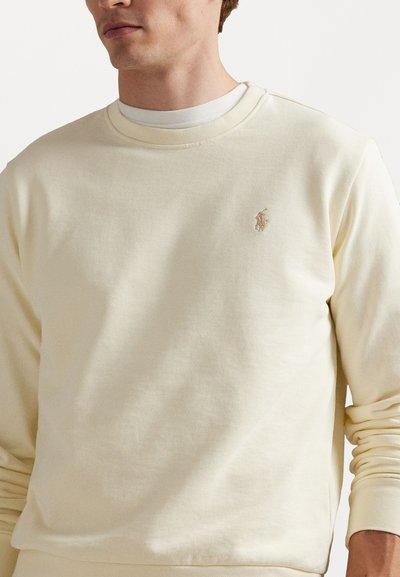 Helles gelbes Sweatshirt aus weichem Stoff, mit langen Ärmeln, einem runden Ausschnitt und einem kleinen gestickten Logo auf der Brust.