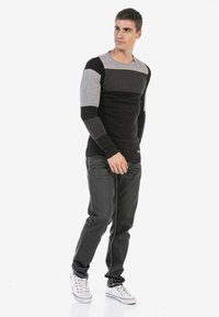 Schwarz-grau gestreifter Langarmpullover mit schmaler Passform, strukturiertem Stoff und rundem Halsausschnitt, kombiniert mit dunklen Jeans und weißen Sneakers.
