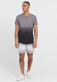 T-shirt gris dégradé à manches courtes, associé à un short de sport gris clair avec des motifs à rayures horizontales. Des baskets blanches complètent le look.