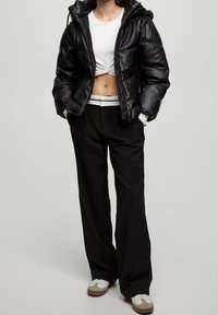 Chaqueta de plumas negra con capucha sobre una blusa corta blanca, combinada con pantalones anchos negros y zapatillas blancas con detalles marrones.