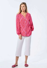 Lange mouwen roze blouse met een diamantpatroon, voorzien van knopen aan de voorkant, gecombineerd met witte crop broeken en roze slide sandalen.