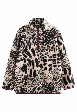 Personne portant un legging noir, des chaussures marron sans lacets avec des chaussettes blanches et un pull pelucheux à motif animalier avec une fermeture éclair au quart.