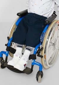Marinblå shorts med knäppning och fickor, båda över vita strumpor med marinblå ränder och vita sneakers, i kombination med en blå rullstol.