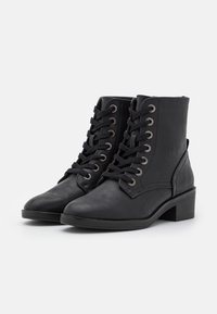 Bottines noires en cuir avec bout arrondi, fermeture à lacets et œillets métalliques. Caractéristiques d'un petit talon carré et d'une texture lisse.