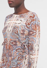 Robe à manches longues avec un motif paisley en bleu, orange et crème. Comprend des liens aux manches et une texture de tissu lisse.