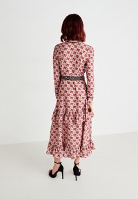 Μάξι φόρεμα με μακριά μανίκια, ροζ ύφασμα με κόκκινο λουλουδάτο σχέδιο, μαύρη ζώνη και βραχίονα με φούστα, σε συνδυασμό με μαύρες ψηλοτάκουνες σαγιονάρες.