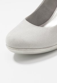 Ljust grå mockapumps med rund tå och en låg, texturerad sula. Släta metalliska inredningsfoder och subtila sömnadsdetaljer.