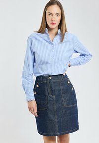 Chemise rayée bleu clair avec un col, associée à une jupe en denim foncé ornée de boutons dorés et de deux poches avant.