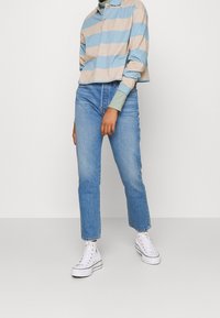 Pale blue and beige striped cropped polo shirt paired with light blue straight-leg jeans and white high-top sneakers.