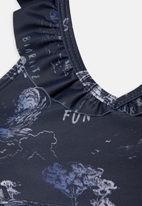 Roupa de banho azul-marinho com parte superior texturizada em ruffles, apresentando um padrão esmaecido em branco de árvores e ondas, e a palavra "DIVERTIDO" integrada no design.