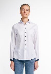 Witte blouse met lange mouwen, knoopsluiting aan de voorkant, marineblauwe accenten op de manchetten en decoratieve knopen. Glad materiaal met een getailleerd ontwerp.