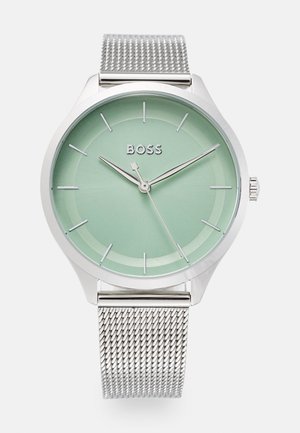 Kulaté stříbrné náramkové hodinky s ocelovým páskem, mátově zeleným ciferníkem, stříbrnými hodinovými značkami a třemi ručičkami ukazujícími čas 10:09:36.